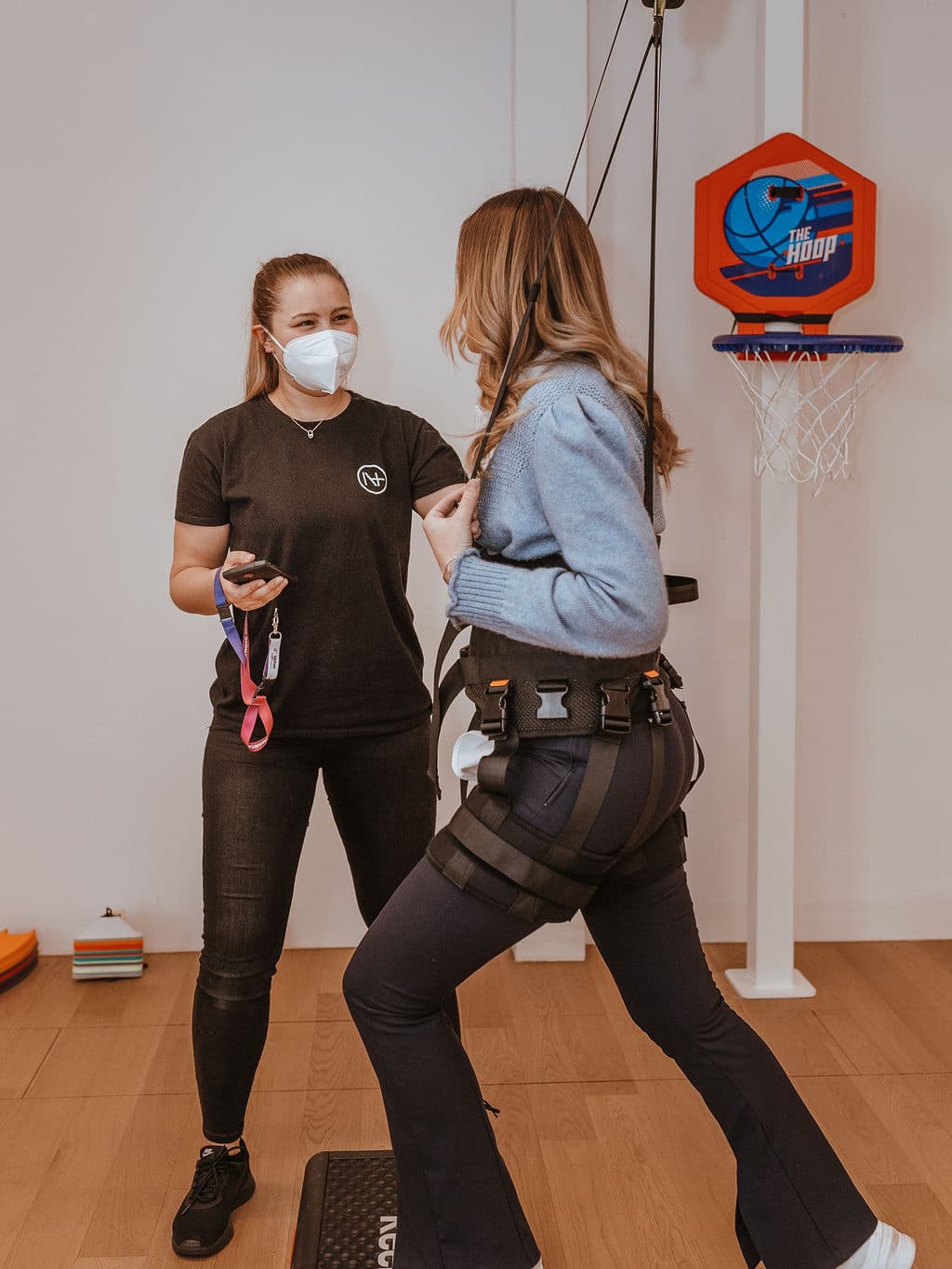 Una paciente entrena con el arnés Rysen delante de una canasta de baloncesto, con una terapeuta