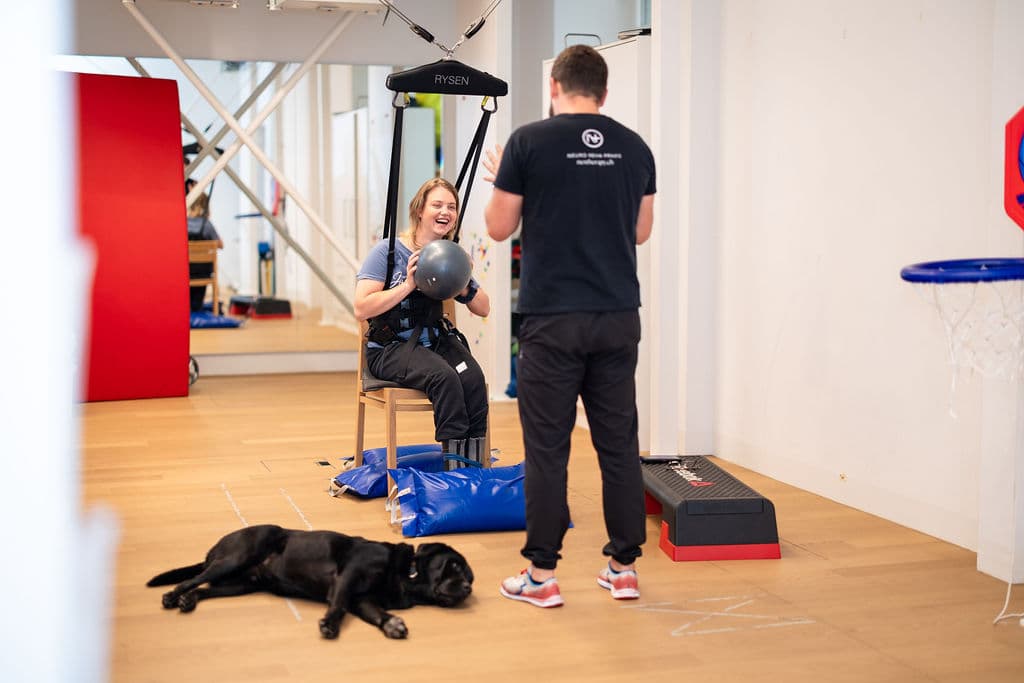 A woman trains in the Rysen harness with a ball, guided by a therapist
